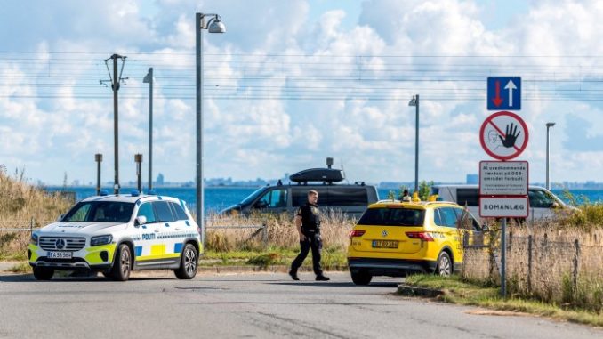 A police officer walks near a police car and a yellow vehicle by a restricted area sign after drones were observed in Danish airspace.
