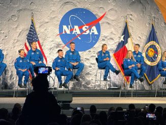 six women and four men, all dressed in blue flight suis, sit on a stage backdropped by images of Earth, the moon and Mars.