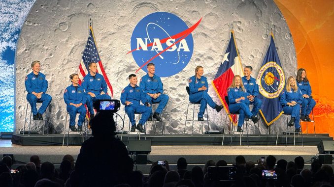 six women and four men, all dressed in blue flight suis, sit on a stage backdropped by images of Earth, the moon and Mars.