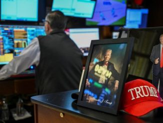 A trader works at a computer surrounded by monitors, with a framed portrait, a cutout of Donald Trump, and a red &quot;TRUMP&quot; hat on the desk.