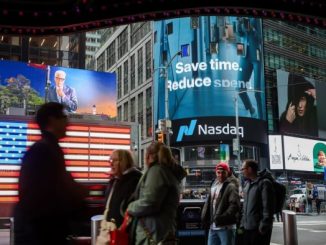 People walk past electronic billboards displaying the Nasdaq logo in New York.