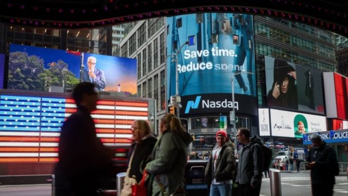 People walk past electronic billboards displaying the Nasdaq logo in New York.