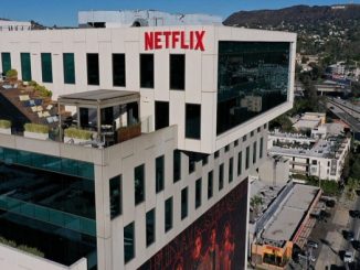 Netflix logo atop Sunset Bronson Studios office building with the Hollywood sign visible in the distant hills.