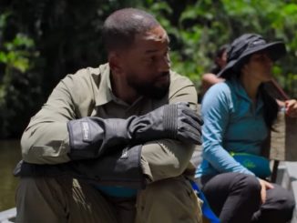 actor will smith in khakis seated with arms folded on is knees in a canoe rowing down a tropical river