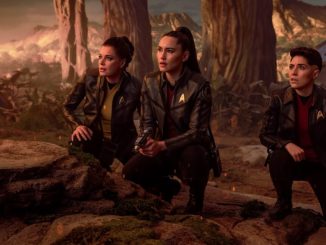 Enterprise crew members on an alien planet hunched down and surveying the terrain