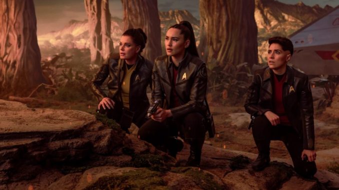 Enterprise crew members on an alien planet hunched down and surveying the terrain