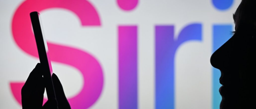 An image of a woman holding a cell phone in front of the Siri logo displayed on a computer screen.