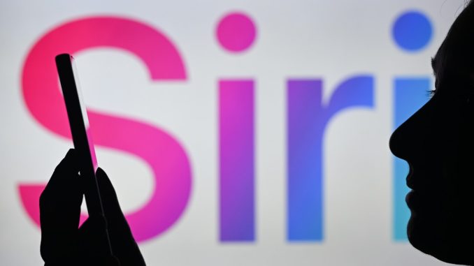 An image of a woman holding a cell phone in front of the Siri logo displayed on a computer screen.