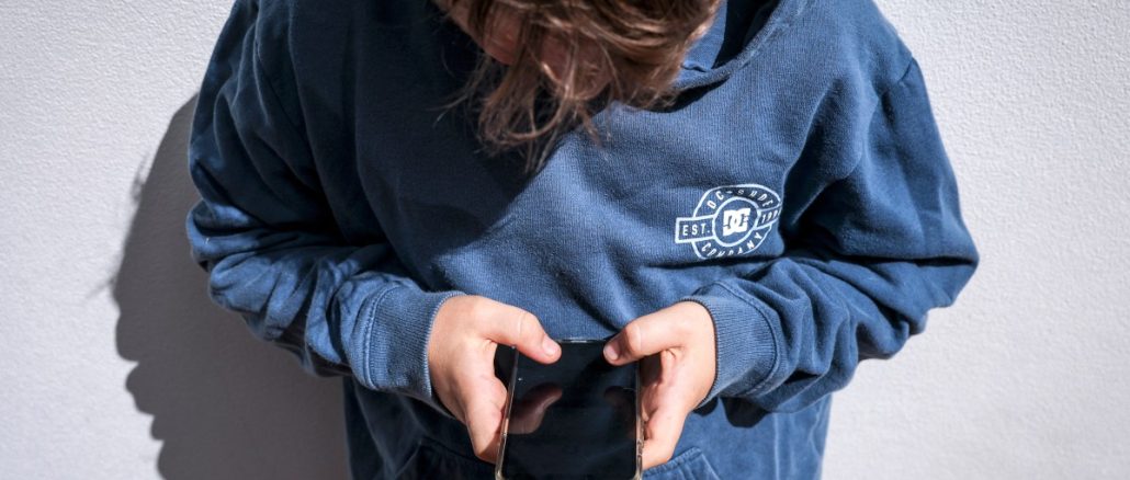 Shows a 14-year-old boy as he looks at social media on his mobile phone.