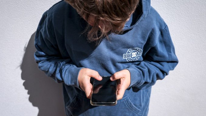 Shows a 14-year-old boy as he looks at social media on his mobile phone.