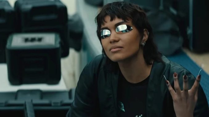 girl with short cropped dark hair wearing futuristic glasses and holding up a hand with long metallic fingernails
